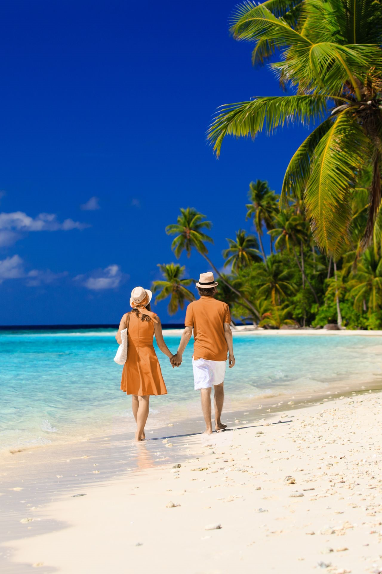 A man and woman walk on the beach holding hands.